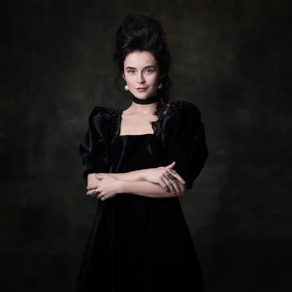 Classic retro portrait of young beautiful woman in image of medieval royal person in black dress isolated on dark vintage background. — Stock Photo, Image