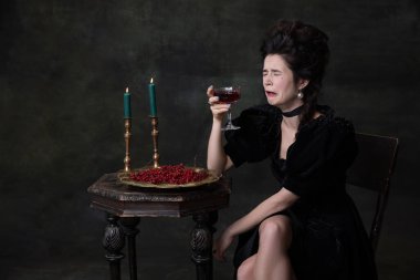 Siyah tatil kıyafetli, yalnız başına şarap içen ve arka planda yalnız başına ağlayan güzel bir kadının yaratıcı portresi..