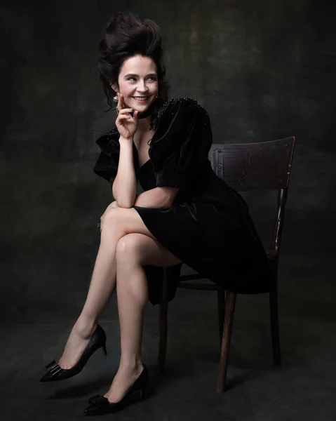 Portrait of young happy woman in image of medieval royal person in black dress isolated on dark vintage background. — Stock Photo, Image