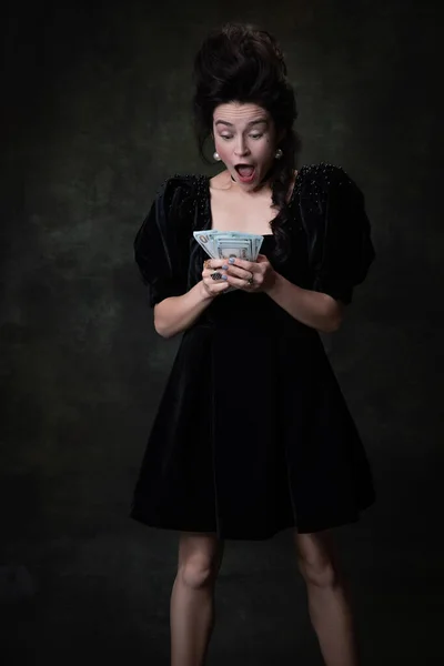 Творческий портрет молодой возбужденной женщины в образе средневековой королевской особы в черном платье, изолированном на темном винтажном фоне. — стоковое фото