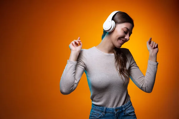 Retrato de meia-comprimento de menina bonita ouvindo música isolada no fundo do estúdio marrom amarelo em luz de néon. — Fotografia de Stock