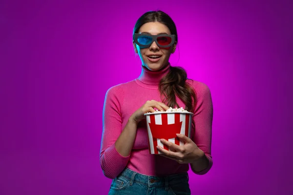 Une jeune belle fille émotionnelle regardant un film isolé sur fond de studio violet dans la lumière rose néon. — Photo
