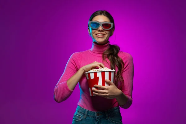 Jeden mladý krásný emocionální dívka sledování film izolovaný na fialové pozadí studia v růžové neonové světlo. — Stock fotografie