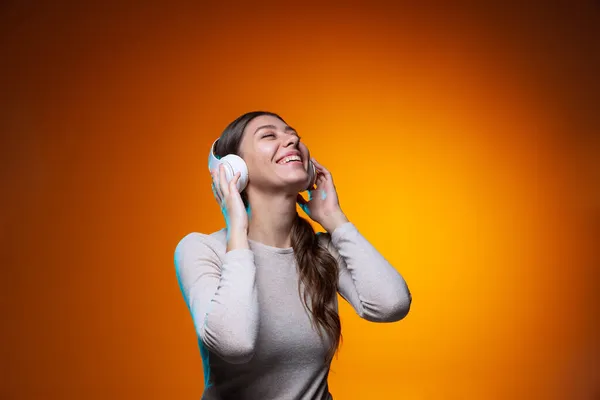 Retrato de meia-comprimento de menina bonita ouvindo música isolada no fundo do estúdio marrom amarelo em luz de néon. — Fotografia de Stock