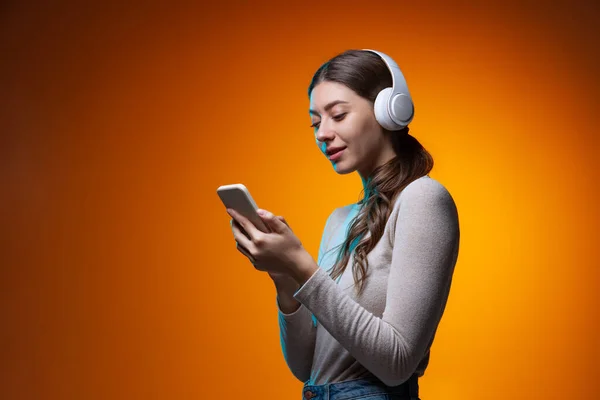 Half-délka portrét mladé krásné dívky poslech hudby a pomocí telefonu izolované na žluté hnědé pozadí studia v neonovém světle. — Stock fotografie