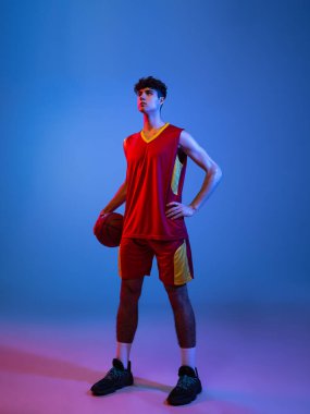 Topla poz veren profesyonel basketbolcunun portresi mavi arka planda neon ışıkta izole edilmiş..