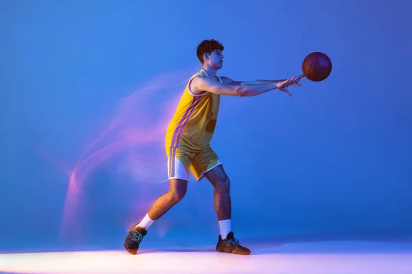 파란색 스튜디오 배경에 혼합 된 네온 빛으로 고립된 공을 가지고 훈련하는 프로 농구 선수의 다이나믹 초상화. — 스톡 사진
