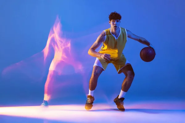 Retrato dinámico de entrenamiento de jugador de baloncesto profesional con pelota aislada sobre fondo de estudio azul en luz de neón mixta. — Foto de Stock