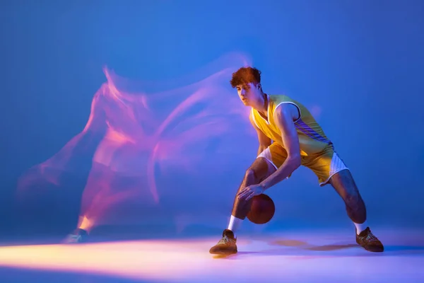 Retrato dinámico de entrenamiento de jugador de baloncesto profesional con pelota aislada sobre fondo de estudio azul en luz de neón mixta. —  Fotos de Stock