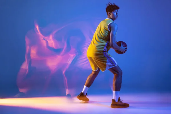 Retrato de larga duración de entrenamiento profesional de jugador de baloncesto con pelota aislada sobre fondo de estudio azul en luz de neón mixta. — Foto de Stock