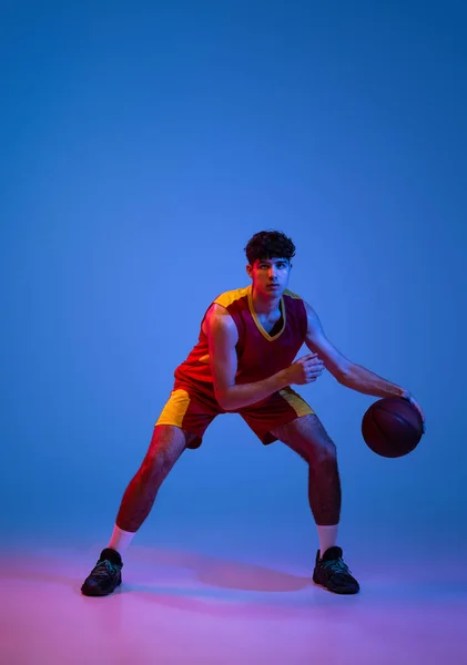 Studio shot of young man, professional basketball player playing basketball isolated on blue background in neon light. — Stock Photo, Image