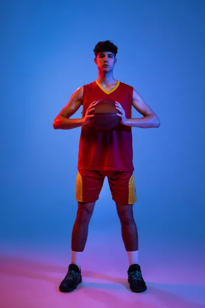 Porträt eines professionellen Basketballspielers, der mit Ball isoliert auf blauem Studiohintergrund in Neonlicht posiert. — Stockfoto