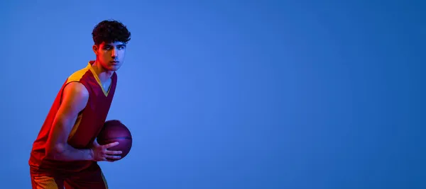 Folheto com jogador de basquete profissional posando com bola isolada no fundo do estúdio azul em luz de néon. — Fotografia de Stock