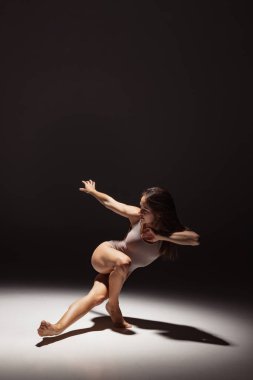 Karanlık stüdyonun arka planında izole edilmiş genç, esnek, düşünceli dansçının dinamik portresi. Sanat, güzellik, ilham konsepti.