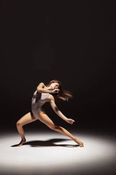 Dynamisches Porträt einer jungen, flexiblen Tänzerin, die isoliert auf dunklem Studiohintergrund im Scheinwerferlicht tanzt. Kunst, Schönheit, Inspirationskonzept. — Stockfoto