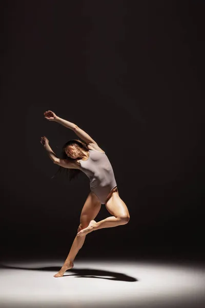 Ritratto dinamico di una giovane ballerina flessibile che danza isolata su uno sfondo scuro da studio sotto i riflettori. Arte, bellezza, concetto di ispirazione. — Foto Stock