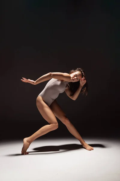 Dynamický portrét mladé ohebné kontemperované tanečnice tančící izolovaně na tmavém pozadí studia ve světle reflektorů. Umění, krása, inspirace. — Stock fotografie