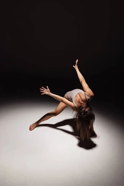 Ritratto dinamico di una giovane ballerina flessibile che danza isolata su uno sfondo scuro da studio sotto i riflettori. Arte, bellezza, concetto di ispirazione. — Foto Stock