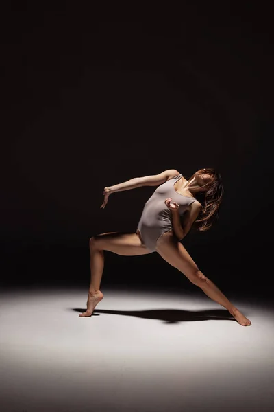 Dynamisch portret van jonge flexibele contemp danser dansen geïsoleerd op donkere studio-achtergrond in de schijnwerpers. Kunst, schoonheid, inspiratie concept. — Stockfoto