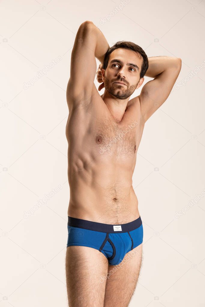 Half-length portrait of young handsome bearded shirtless man standing alone isolated on white studio background.