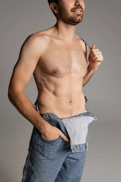 Portrait de jeune homme barbu torse nu en jeans posant isolé sur fond de studio gris. — Photo