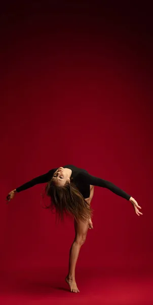 Studio shot di giovane ragazza flessibile, ballerina accompagnatrice femminile, ballerina in azione isolata su sfondo rosso scuro. Arte, bellezza, concetto di ispirazione. — Foto Stock