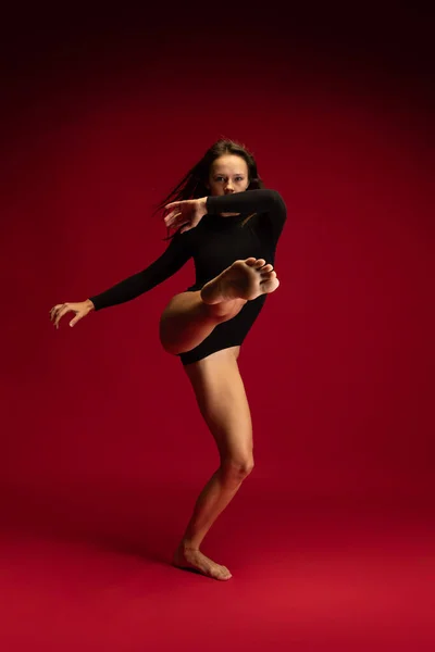 Eine emotionale junge, flexible Kandidatentänzerin, Ballerina, die isoliert auf dunkelrotem Hintergrund springt. Kunst, Schönheit, Inspirationskonzept. — Stockfoto