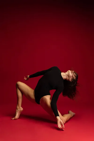 ダークレッドの背景に孤立した若い柔軟なコンテンポラリーダンスのダイナミックなポートレート。芸術、美、インスピレーションの概念. — ストック写真