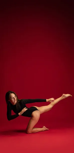 Eine emotionale junge, flexible Tänzerin, Ballerina, die isoliert auf dunkelrotem Hintergrund tanzt. Kunst, Schönheit, Inspirationskonzept. — Stockfoto