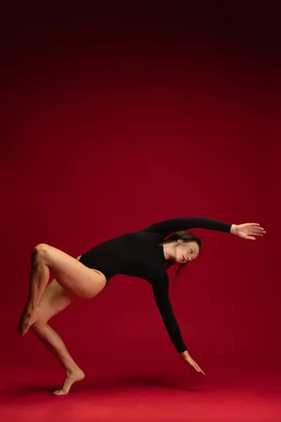 ダークレッドの背景に孤立した若い柔軟なコンテンポラリーダンスのダイナミックなポートレート。芸術、美、インスピレーションの概念. — ストック写真