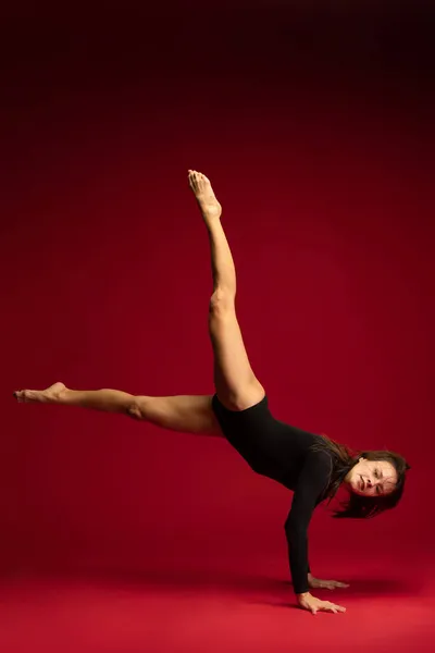Studio bild av ung flexibel flicka, kvinnlig samtida dansare, ballerina i aktion isolerad på mörkröd bakgrund. Konst, skönhet, inspiration koncept. — Stockfoto