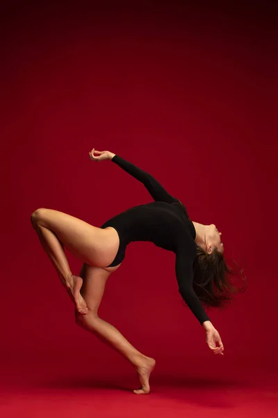 Porträtt av emotionell ung flexibel samtida dansare, ballerina dans isolerad på mörkröd bakgrund. Konst, skönhet, inspiration koncept. — Stockfoto