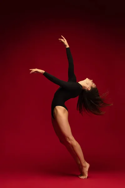 Одна эмоциональная молодая гибкая танцовщица, балерина танцует изолированно на темно-красном фоне. Искусство, красота, вдохновение. — стоковое фото