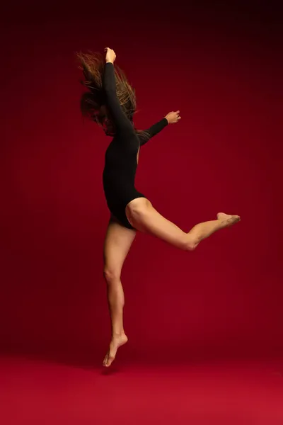 Dynamiczny portret młodego elastycznego tancerza kontemplacyjnego tańczącego na ciemnoczerwonym tle. Sztuka, piękno, koncepcja inspiracji. — Zdjęcie stockowe