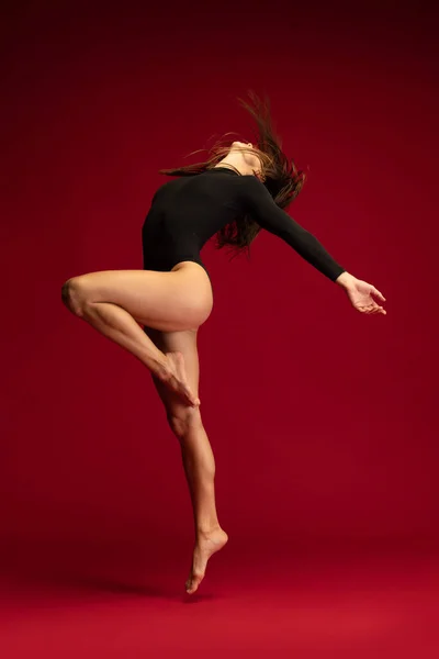 Jedna emocjonalna młoda, elastyczna tancerka kontemplacyjna, tańcząca balerinę na ciemnoczerwonym tle. Sztuka, piękno, koncepcja inspiracji. — Zdjęcie stockowe