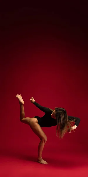 Ritratto dinamico di una giovane ballerina flessibile che danza isolata su sfondo rosso scuro. Arte, bellezza, concetto di ispirazione. — Foto Stock
