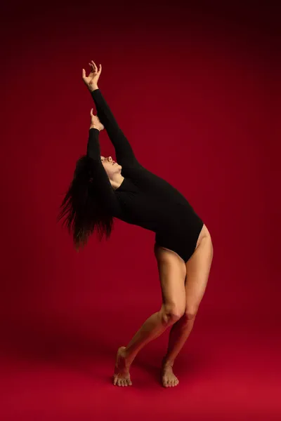 暗い赤の背景に隔離された1つの感情的な若い柔軟な現代舞踊家、バレリーナダンス。芸術、美、インスピレーションの概念. — ストック写真