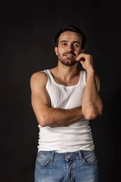 Retrato clássico de jovem bonito barbudo homem triste em camiseta branca e jeans isolado no fundo escuro. Emoções, expressão facial — Fotografia de Stock