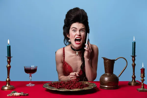 Retrato de jovem adorável linda mulher em vermelho escuro, vestido de noite cor de vinho falando no telefone isolado no fundo azul. — Fotografia de Stock