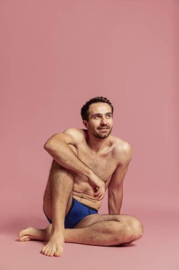 Stüdyoda, pembe arka planda, mavi külotlu, sakalsız, genç ve yakışıklı bir adamın görüntüsü..