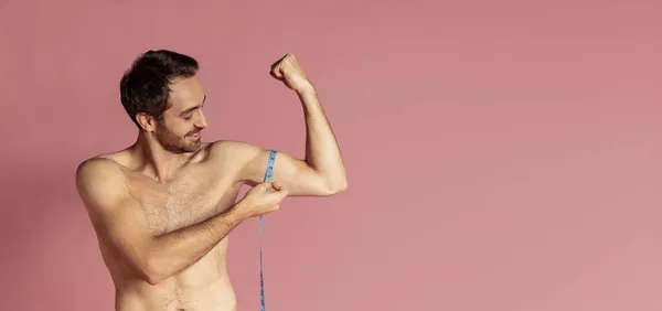 Flyer nuori lihaksikas komea parrakas paidaton mies mittaamalla hänen hauikset eristetty vaaleanpunainen studio tausta. — kuvapankkivalokuva