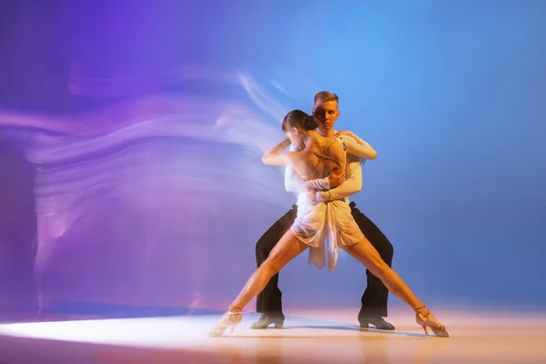 Dynamisch portret van sierlijke dansers, flexibele man en vrouw dansen ballroom dans geïsoleerd op gradiënt blauw paarse achtergrond in neon gemengd licht — Stockfoto