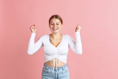 Gülümseyen sevimli çilli bir kız elini kaldırır ve pembe stüdyo arka planında izole edilmiş bir şekilde neşelenir. Duyguların kavramı,