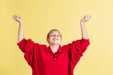 Gülümseyen sevimli çilli bir kız elini kaldırır ve sarı stüdyo arka planında izole edilmiş bir şekilde neşelenir. Duyguların kavramı,