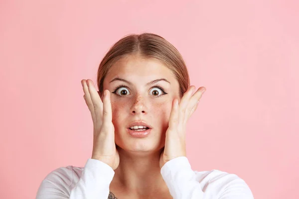 Nahaufnahme Porträt eines jungen schockierten Mädchens mit niedlichen Sommersprossen, das mit großen Augen in die Kamera blickt, isoliert auf rosa Studiohintergrund. — Stockfoto