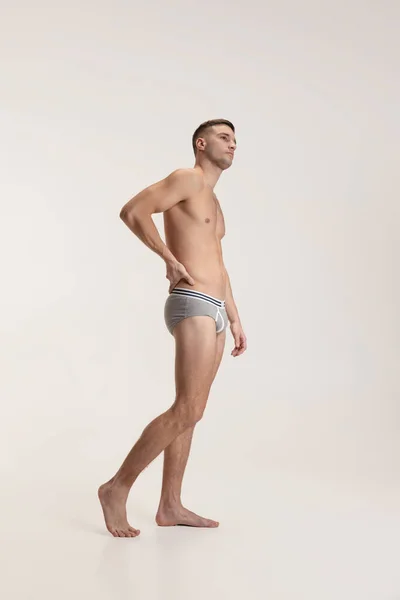 Studio shot van jonge knappe sportieve shirtloze man in ondergoed geïsoleerd op grijze studio achtergrond. — Stockfoto
