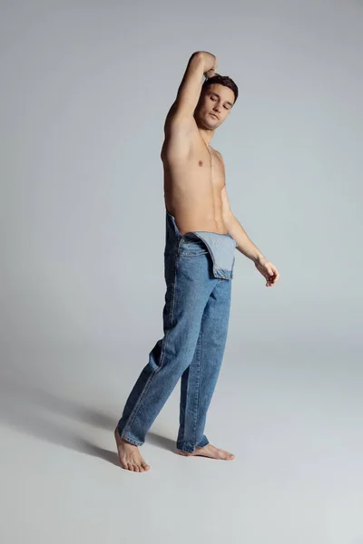 Портрет молодого красивого спортсмена без сорочки в джинсах позує ізольовано на сірому студійному фоні . — стокове фото