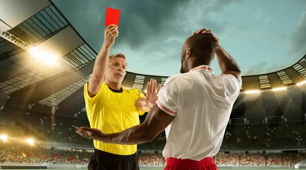 Футбольний арбітр, який показує гравцеві червону картку за порушення правил на переповненому стадіоні над нічним хмарним небом . — стокове фото