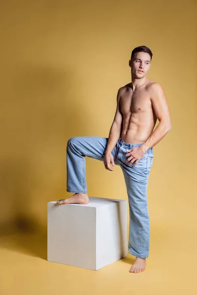 黄色のスタジオの背景に隔離されたポーズ青いジーンズの健康な若い無気力な男。カジュアルファッションコレクション — ストック写真