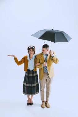 Genç üzgün aile çifti, 70 'ler, 60' lar modası modasında beyaz stüdyo arka planında izole edilmiş şemsiyeyle yürüyen erkek ve kadın.